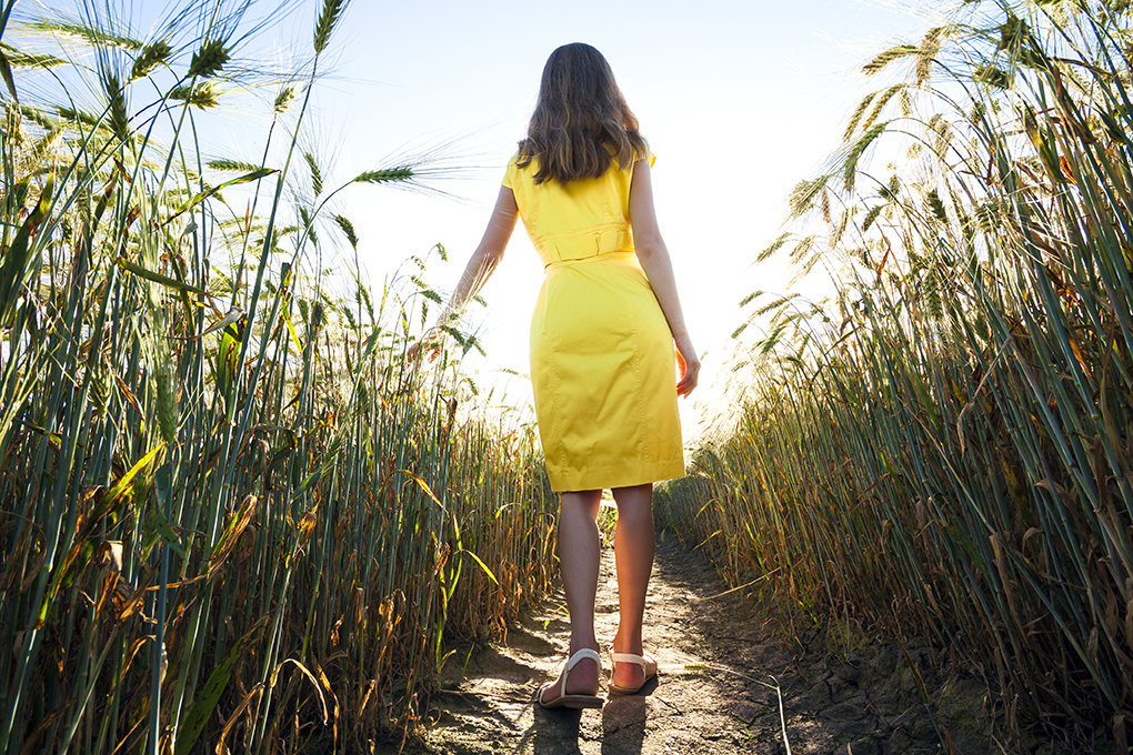 Beauty young girl outdoors enjoying nature. Beautiful teenage model girl in yellow dress walking on the wheat field in sun light.