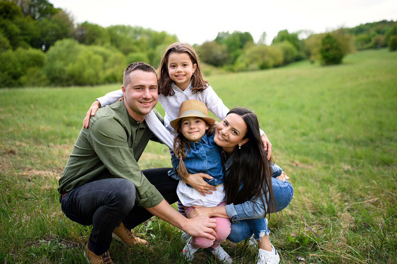 Happy family with two small daughters sitting outdoors in spring nature, looking at camera.