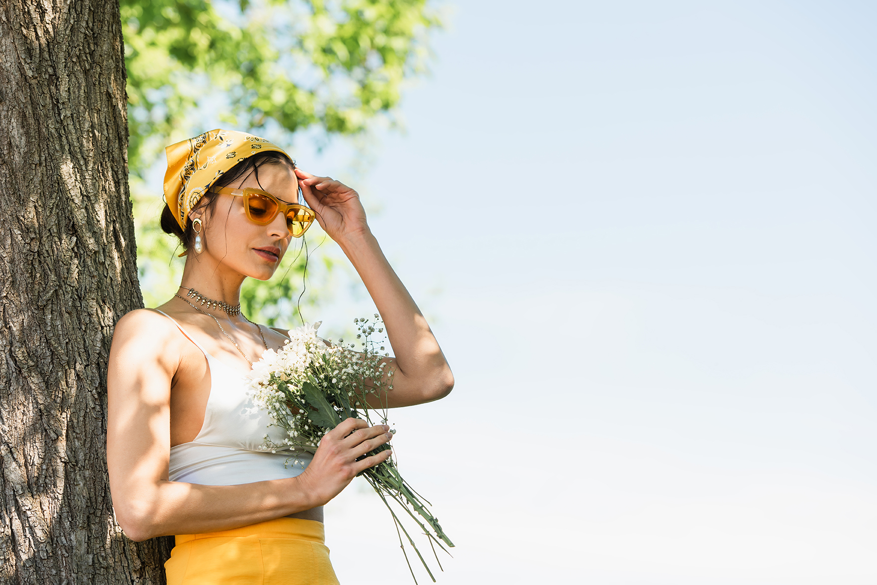 trendy woman in sunglasses and yellow headscarf holding flowers